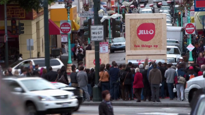 Photo of crowd on street corner surrouncing crates of Jell-O pudding cups.